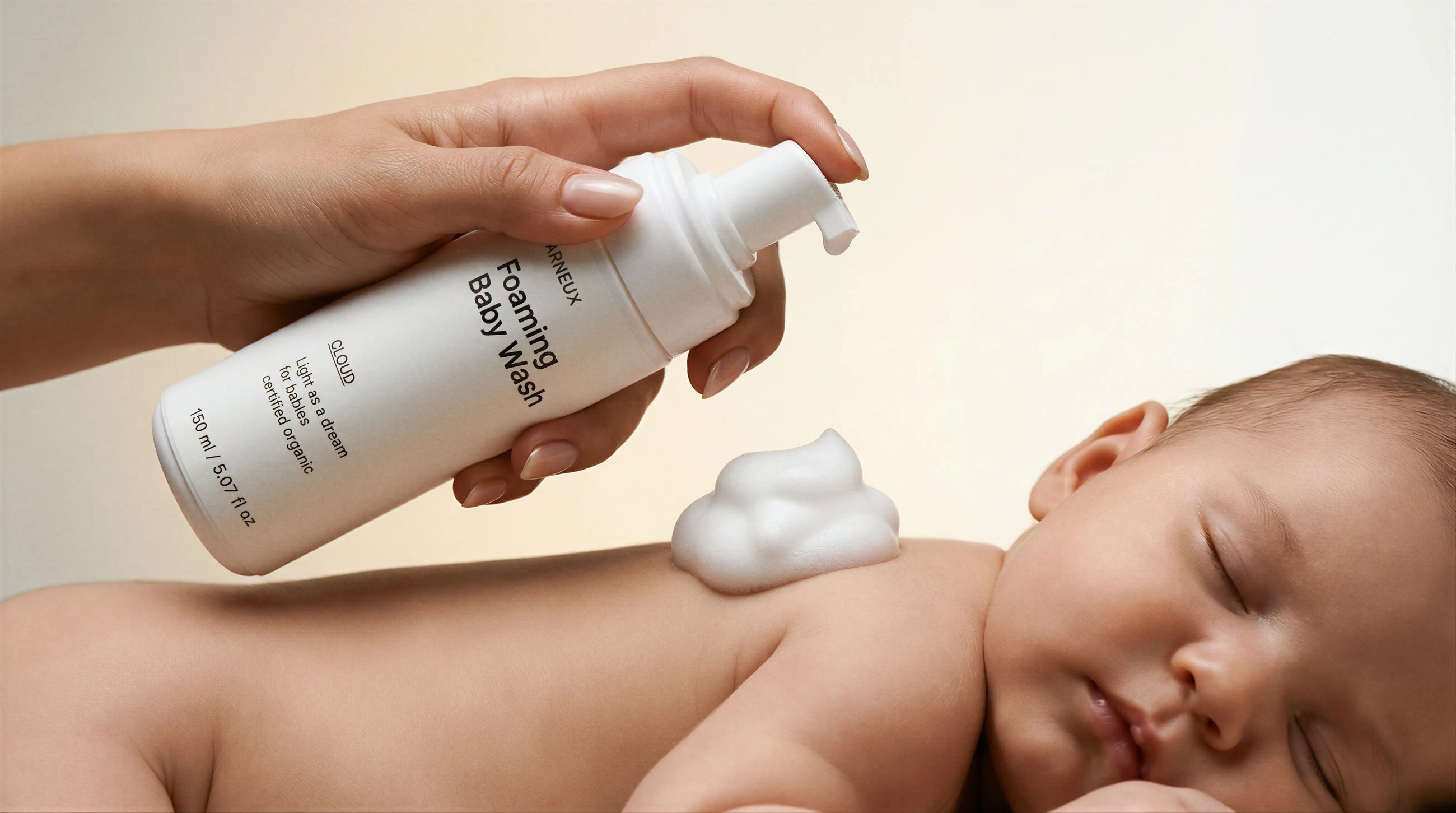 Adult hands dispensing CLOUD foaming baby wash foam onto sleeping newborn's head, gentle from day one