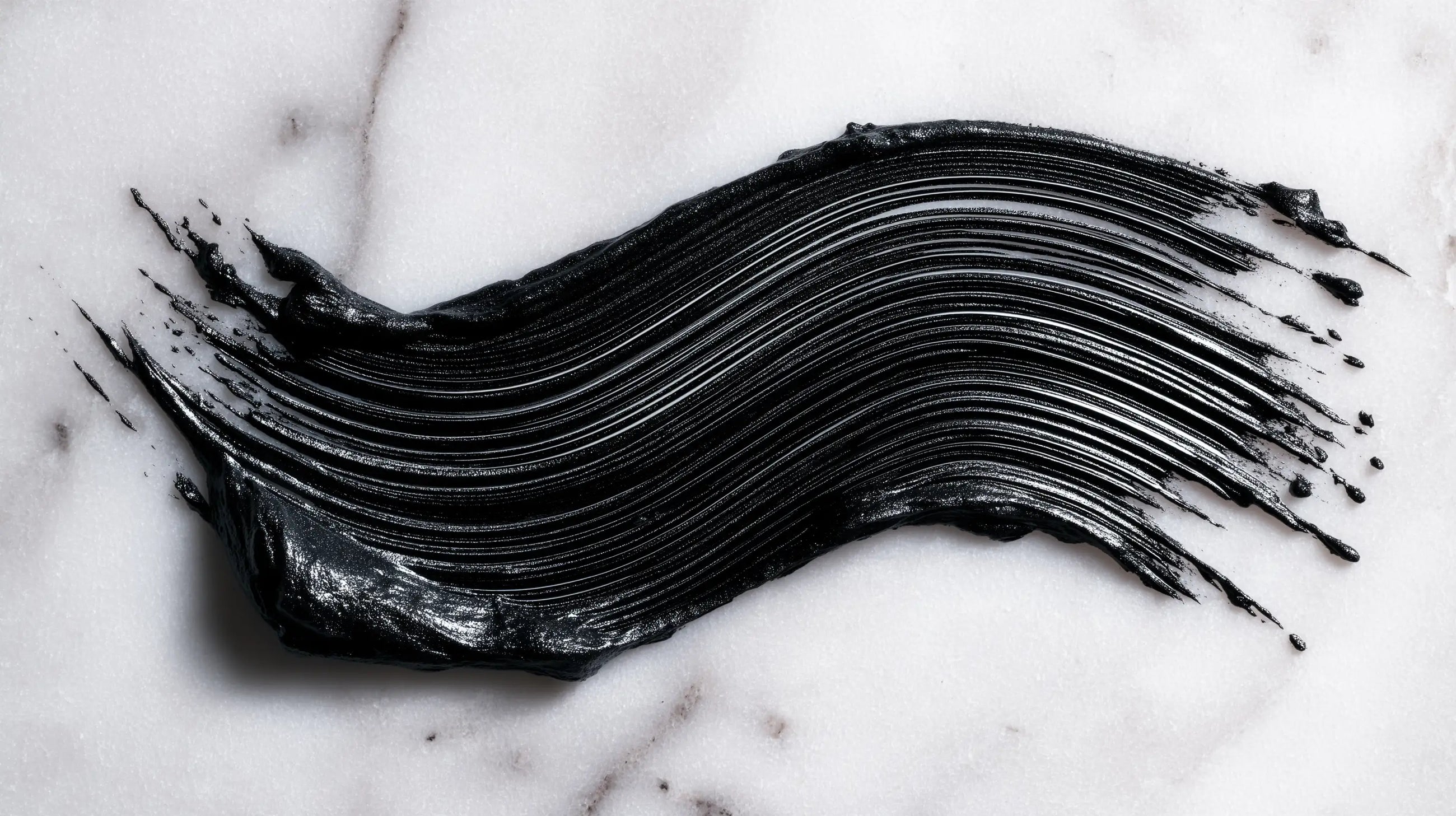 Intense black mascara formula swatch smeared on white marble, showing pigment depth and texture