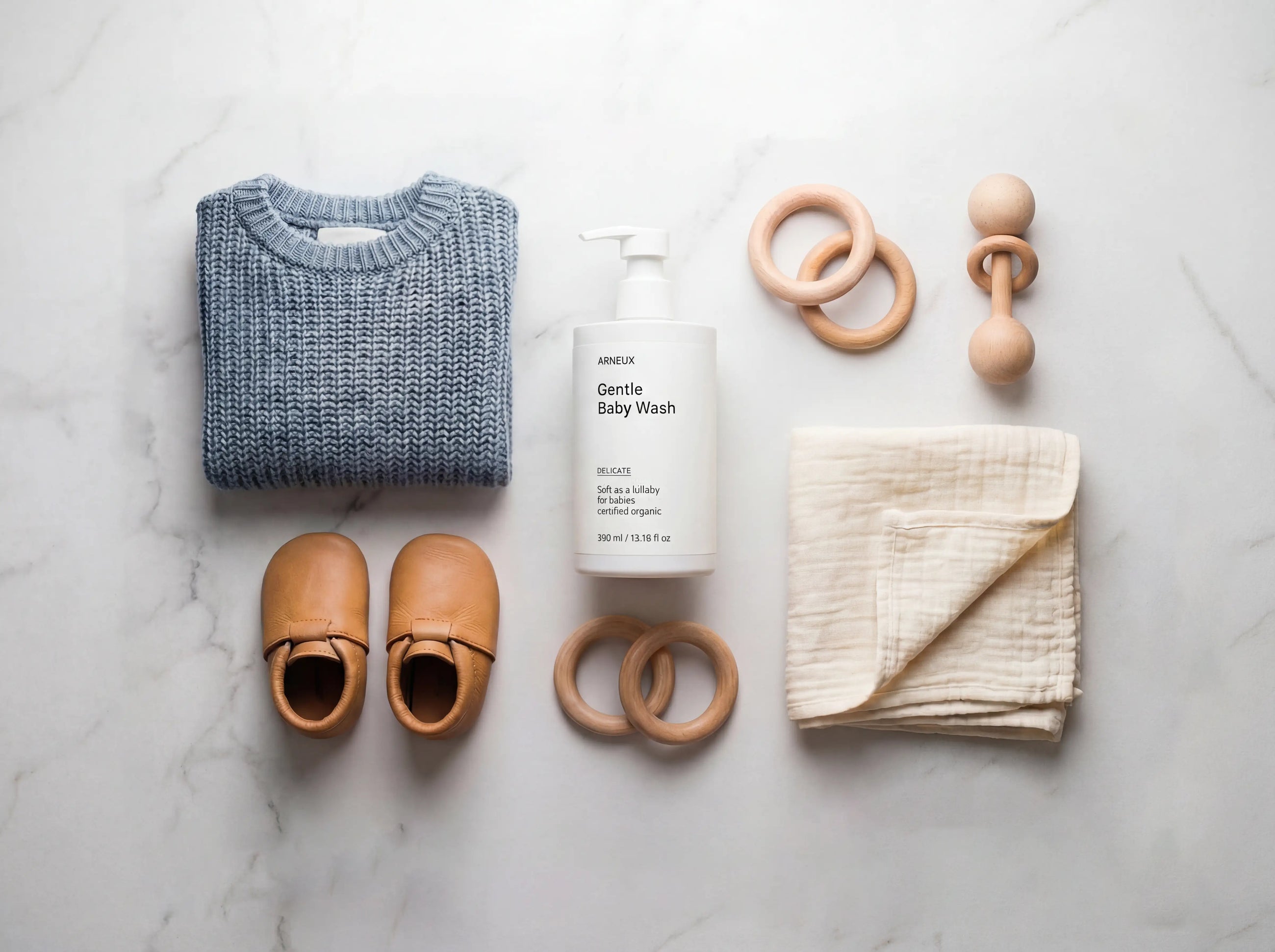 DELICATE gentle baby wash flatlay with folded sweater, leather baby shoes and wooden toys on white marble
