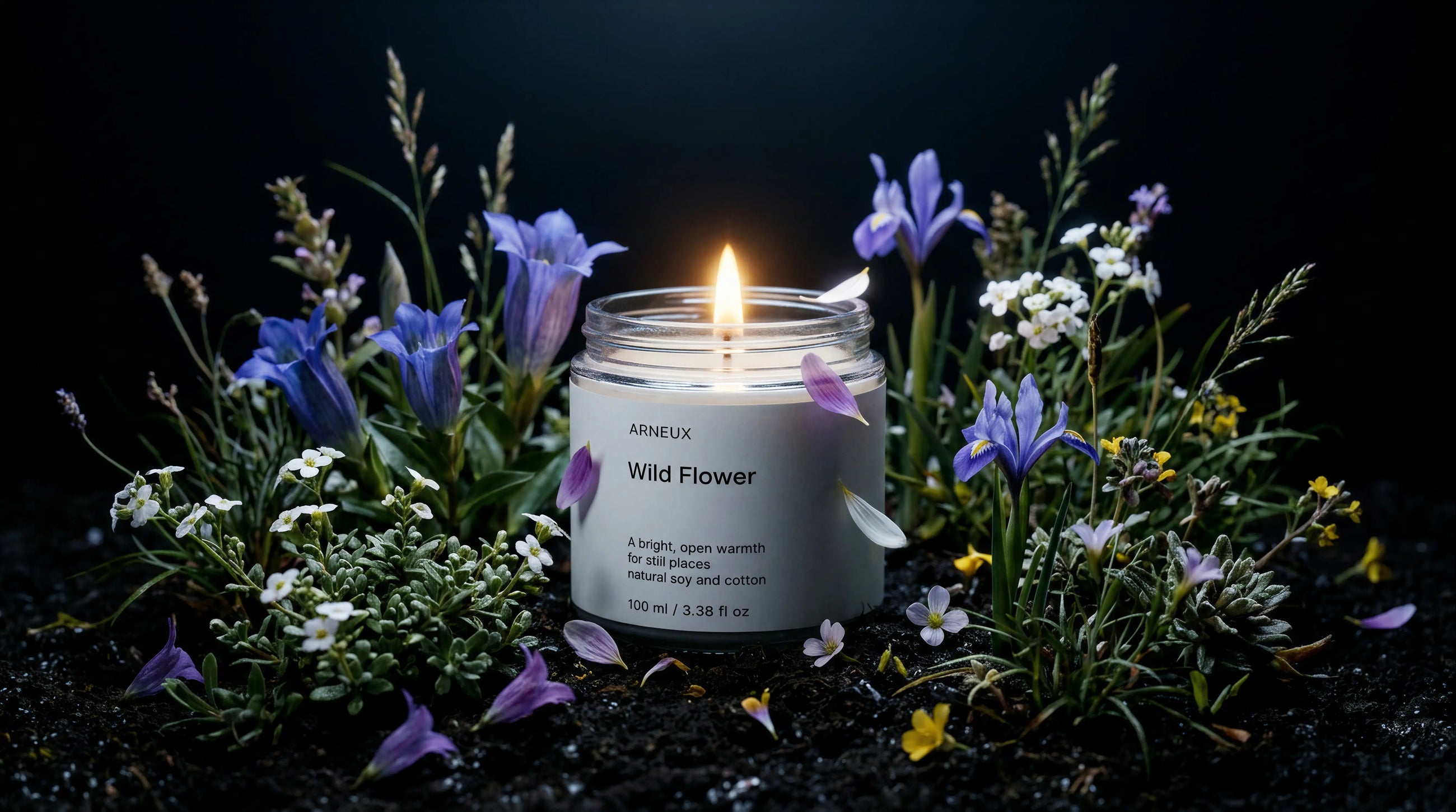 WILD FLOWER travel candle burning among purple iris, white blossoms and wild meadow grasses on dark background