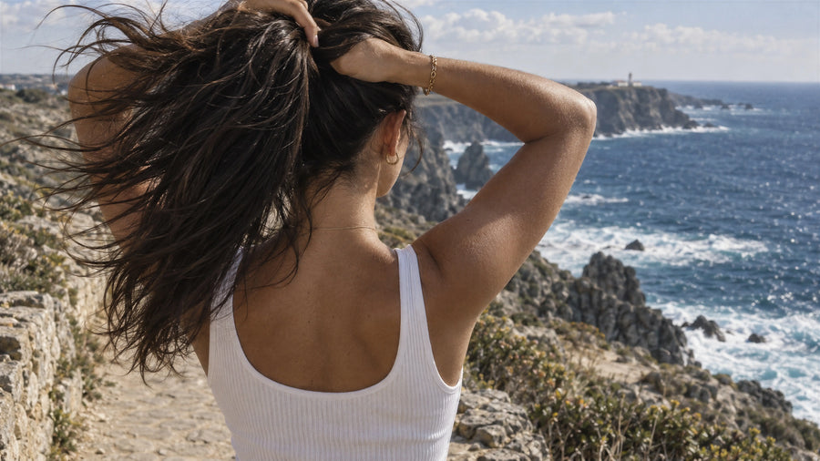 Woman gathering her thick, healthy dark hair into a ponytail on a windswept coastal path