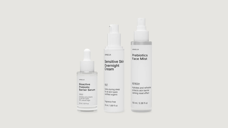 Three white ARNEUX cosmetic bottles on a light gray background: Bioactive Prebiotic Barrier Serum, Sensitive Skin Overnight Cream, and Prebiotics Face Mist