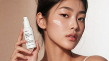 A close-up of a woman holding a white bottle of ARENUX Retinol Alternative Serum, with a swipe of white serum on her cheek against a warm beige background