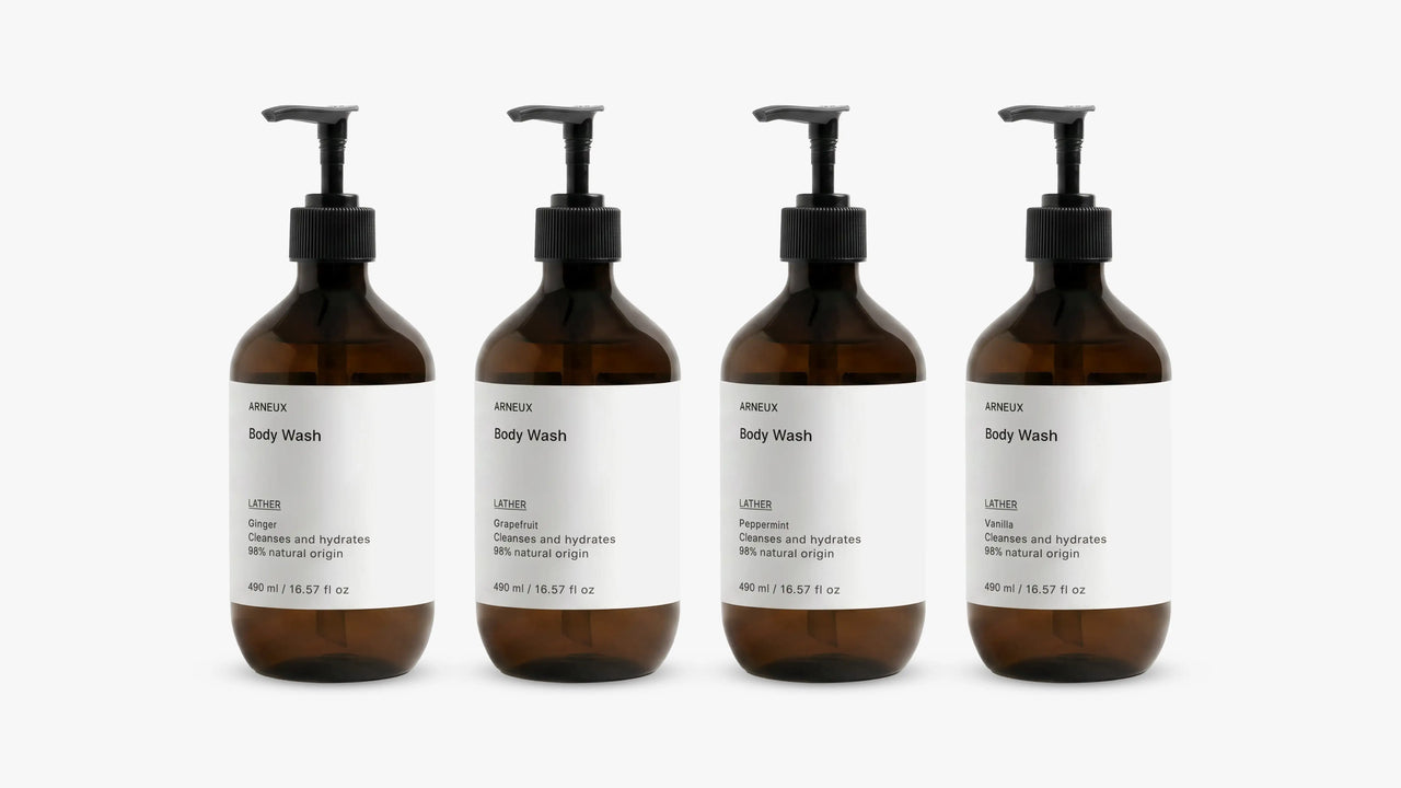 INDULGE The Shower Edit by ARNEUX, four organic body wash scents in amber bottles on white background