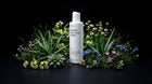 BARE micellar cleansing water bottle nestled in aloe and wildflowers on black background