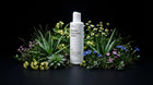 BARE micellar cleansing water bottle nestled in aloe and wildflowers on black background