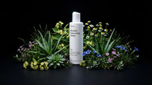 BARE micellar cleansing water bottle nestled in aloe and wildflowers on black background