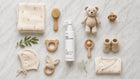 CARE baby body lotion flatlay with teddy bear, wooden toys, swaddle blanket and booties on white marble
