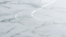 A close-up of a clear ARNEUX natural deodorant swipe on a white and gray marble surface