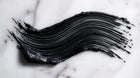 Intense black mascara formula swatch smeared on white marble, showing pigment depth and texture