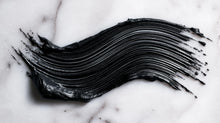 Intense black mascara formula swatch smeared on white marble, showing pigment depth and texture