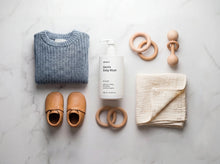 DELICATE gentle baby wash flatlay with folded sweater, leather baby shoes and wooden toys on white marble