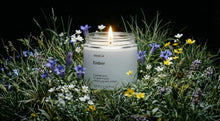 EMBER travel candle burning in wild meadow surrounded by purple white and yellow wildflowers at dusk