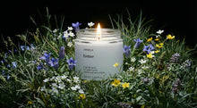 EMBER travel candle burning in wild meadow surrounded by purple white and yellow wildflowers at dusk