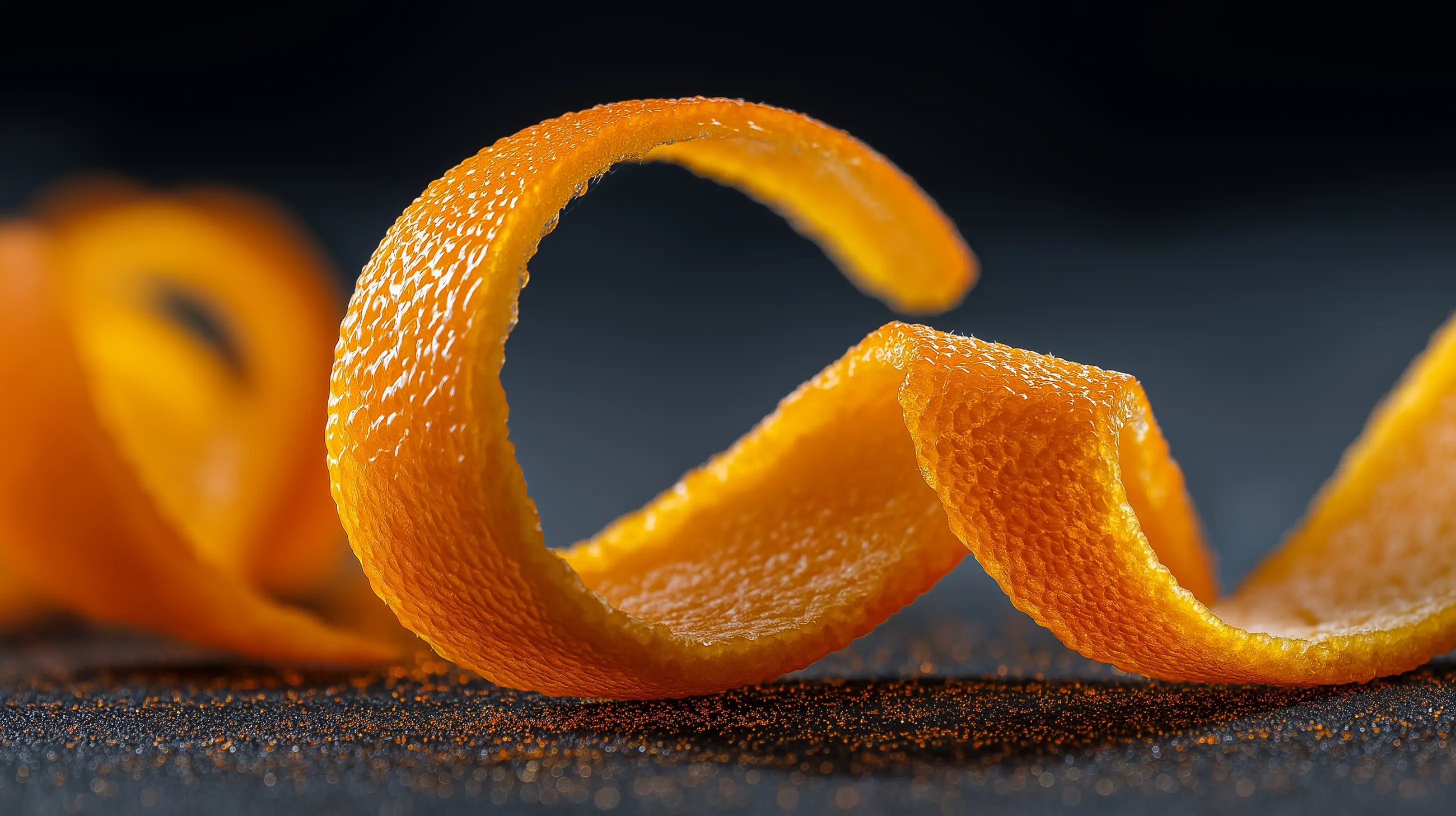 Curled fresh orange peel close-up on dark surface, vitamin C citrus ingredient in EVEN dark spot cream