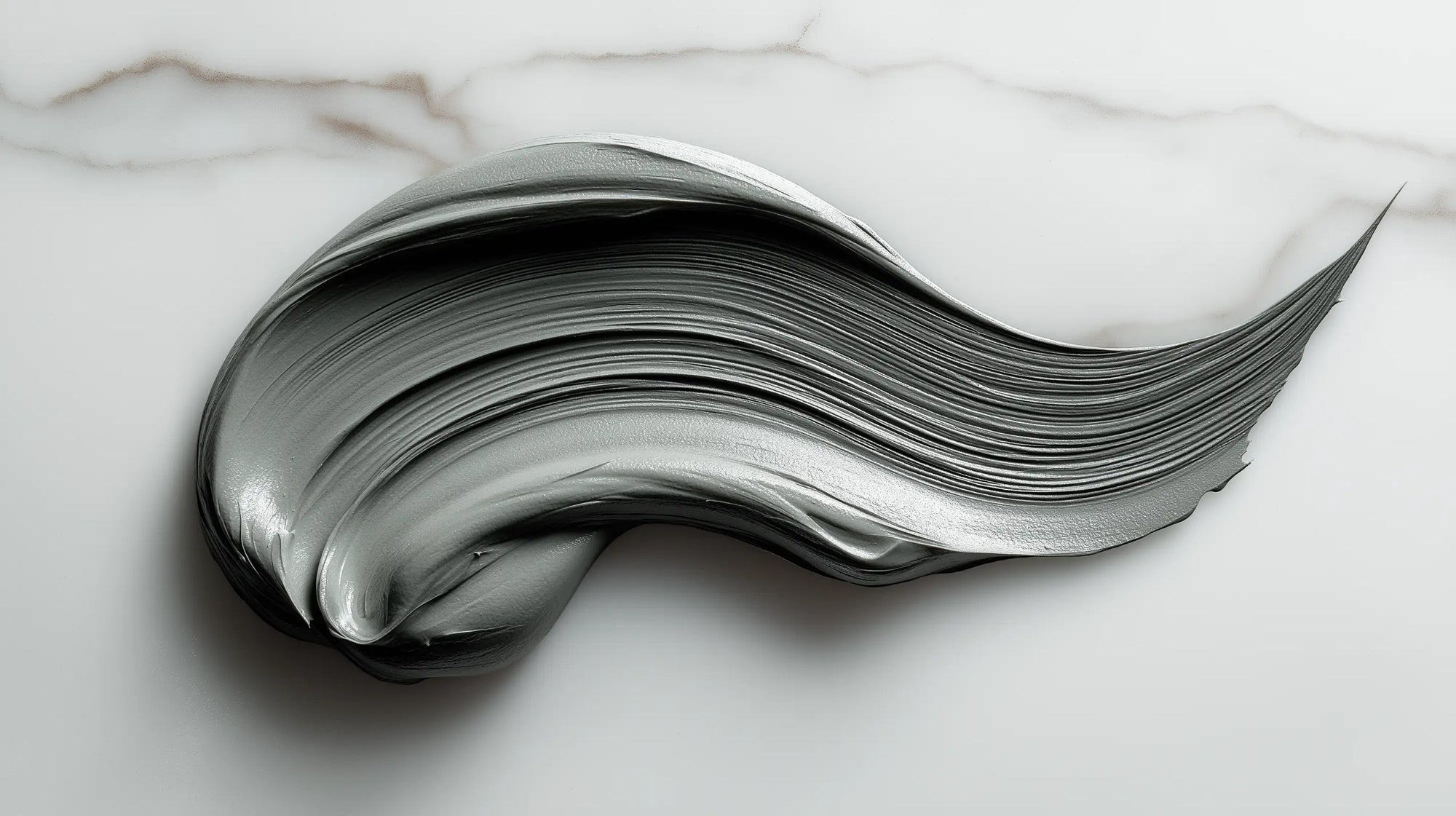 Grey-green purifying clay mask texture swiped on white marble showing dense smooth consistency