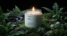 MOSS travel candle burning on mossy forest floor surrounded by ferns and blue wildflowers