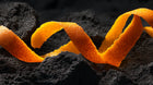Curled orange peel on dark volcanic rock, brightening citrus ingredient in REFINE face and body scrub