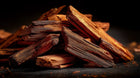 Stacked sandalwood wood sticks on dark surface, conditioning aromatic ingredient in ROOT rosemary hair oil