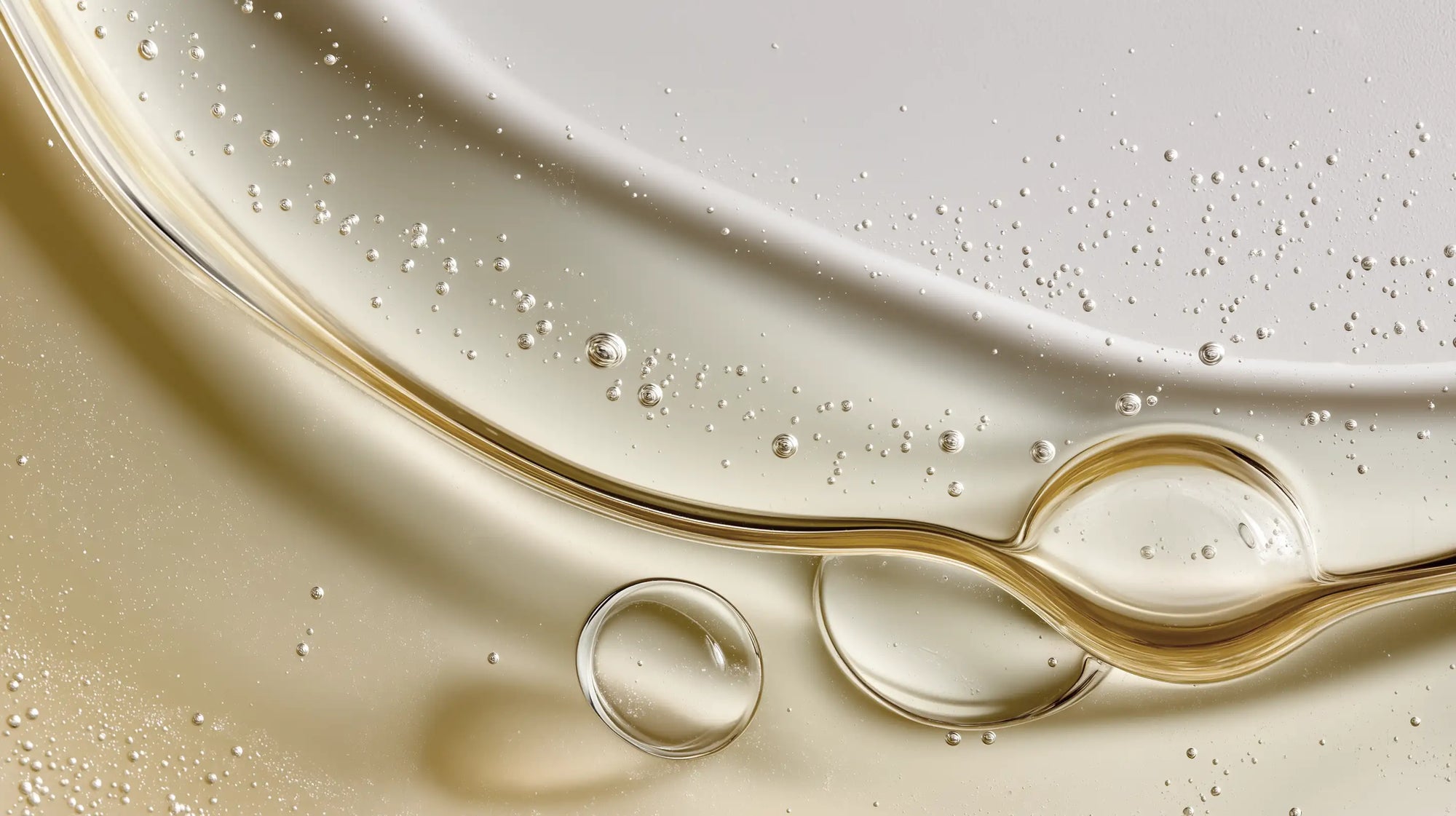 Golden rosemary hair oil swirling on surface with fine droplets, lightweight concentrated formula texture
