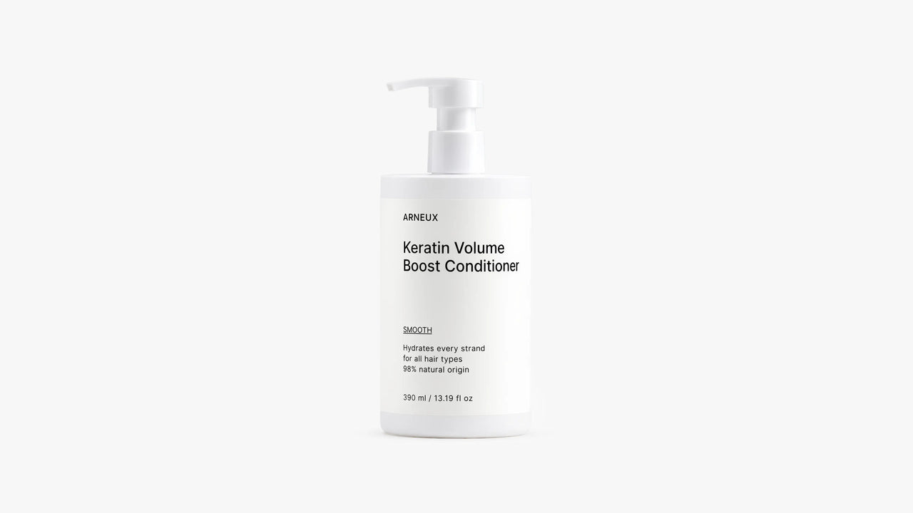 A white pump bottle of Arneux Keratin Volume Boost Conditioner, photographed against a seamless light gray studio background