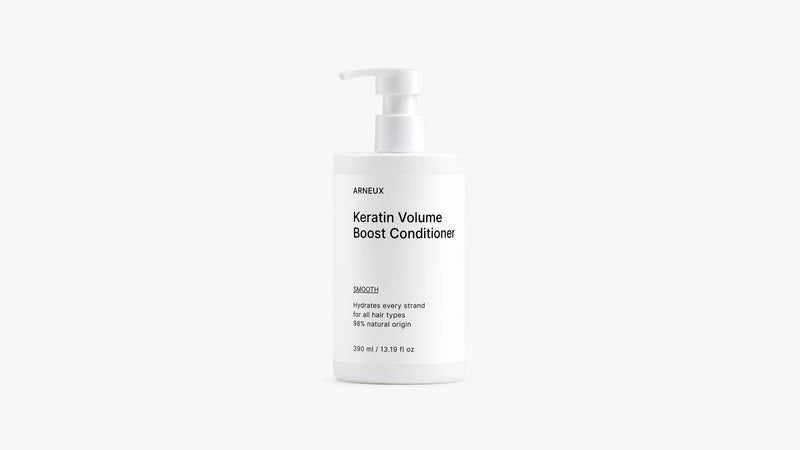 A white pump bottle of Arneux Keratin Volume Boost Conditioner, photographed against a seamless light gray studio background