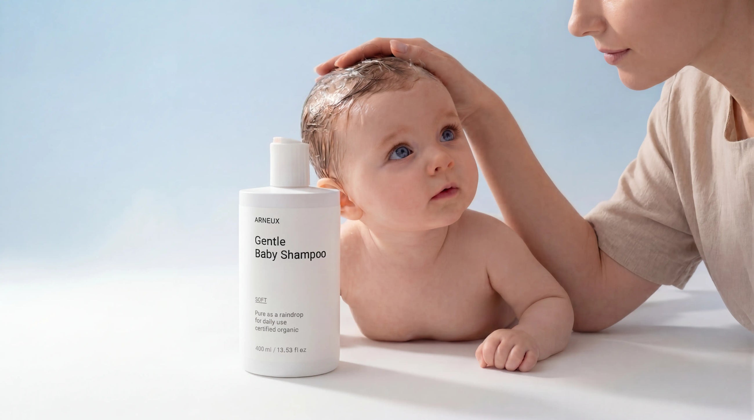 Baby lying on white surface with parent holding SOFT gentle baby shampoo, COSMOS certified newborns and up
