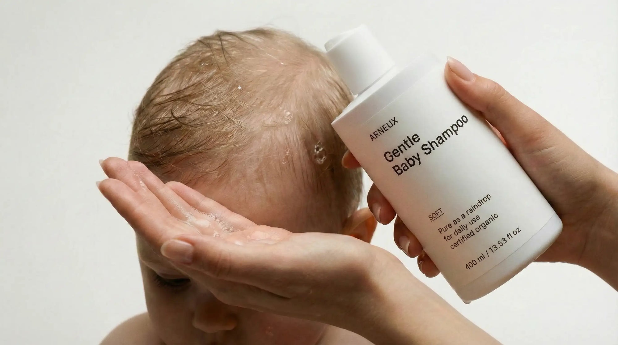 Adult hands washing newborn's fine hair with SOFT gentle baby shampoo, tear-free safe from birth