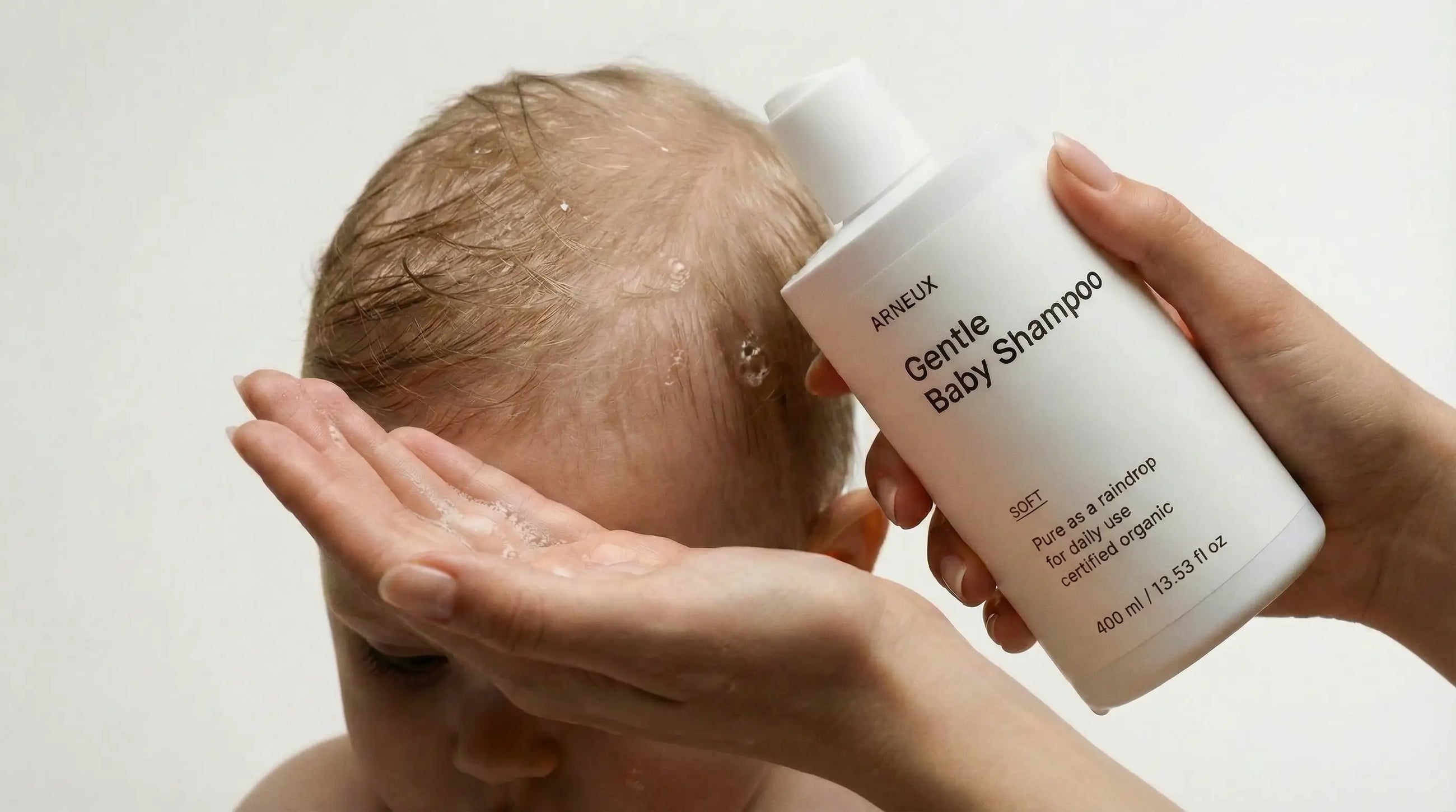 Adult hands washing newborn's fine hair with SOFT gentle baby shampoo, tear-free safe from birth