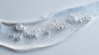 Keratin volume boost shampoo clear gel with bubbles on grey surface, sulfate-free lather texture