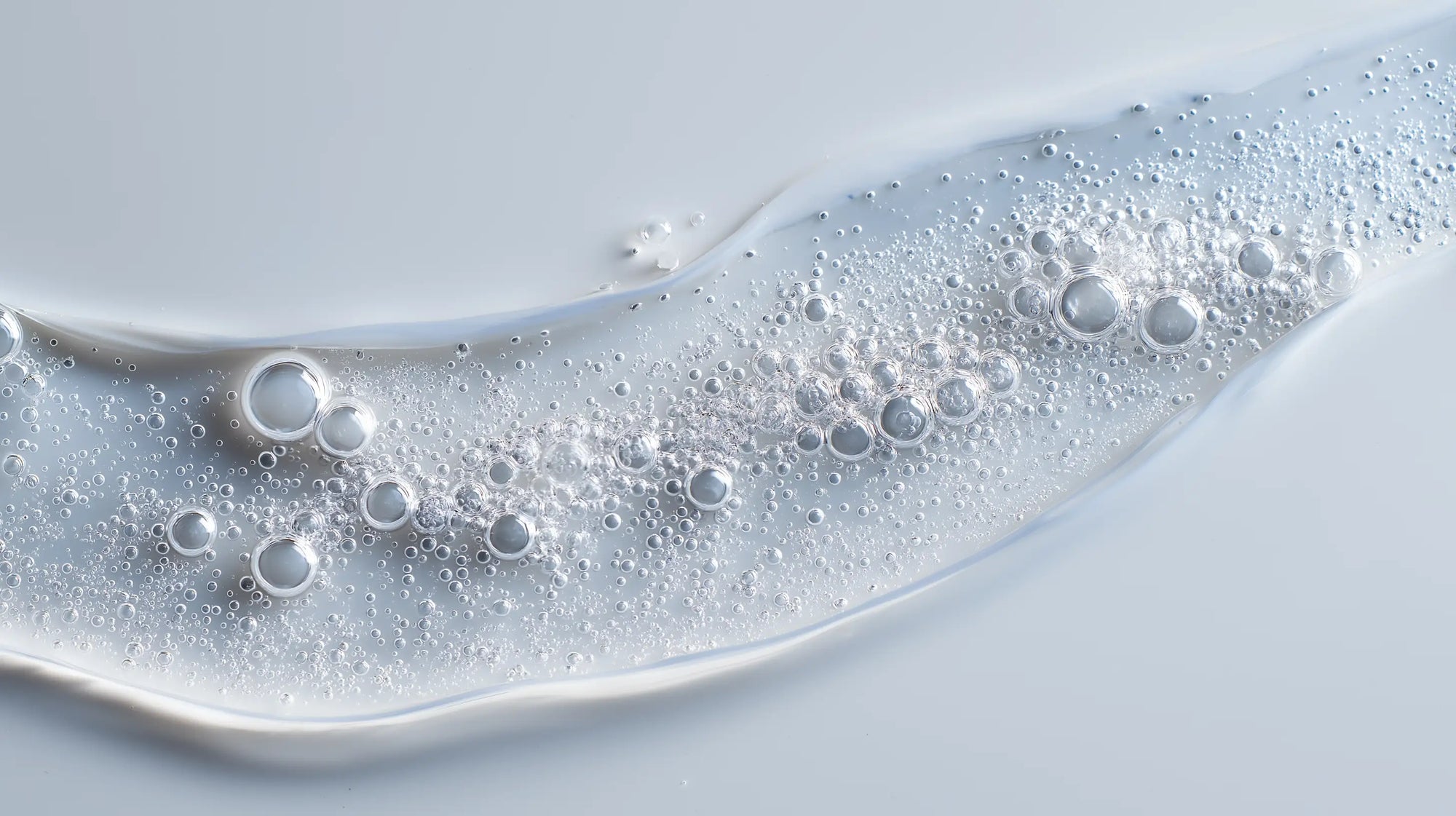 Keratin volume boost shampoo clear gel with bubbles on grey surface, sulfate-free lather texture