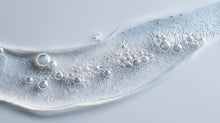 Keratin volume boost shampoo clear gel with bubbles on grey surface, sulfate-free lather texture