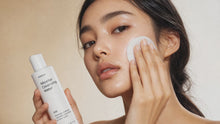 Woman sweeping cotton pad across cheek with micellar cleansing water, close-up skin texture view