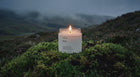 MOSS soy wax travel candle burning on vivid green moss bed in dramatic misty highland landscape