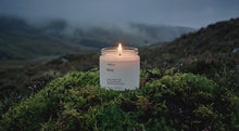 MOSS soy wax travel candle burning on vivid green moss bed in dramatic misty highland landscape