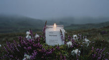 WILD FLOWER soy wax candle glowing among purple heather and cotton grass in misty highland landscape
