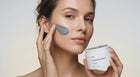 Woman smoothing FLAWLESS purifying clay mask across face with fingertips, jar held in hand