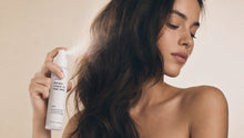Woman misting TAME keratin spray through long dark hair, smooth glossy finish side profile view