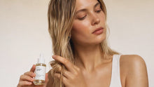 Woman running fingers through glossy hair holding ROOT rosemary hair oil, natural shine and softness