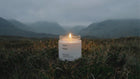 EMBER soy wax travel candle burning alone in dramatic moody Scottish highlands landscape at dusk