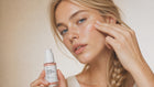 Woman dotting REVIVE peptide serum onto cheekbone with fingertip, dewy firm skin close-up