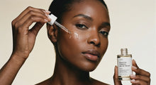 Woman dropping SHIELD prebiotic barrier serum onto cheekbone, clear serum absorbing into skin