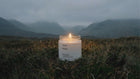 EMBER soy wax travel candle burning alone in dramatic moody Scottish highlands landscape at dusk