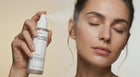 Woman with eyes closed spritzing prebiotic face mist, dewy refreshed skin close-up